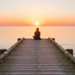 Person on pier at sunset, representing seeking help for depression and mental wellness.